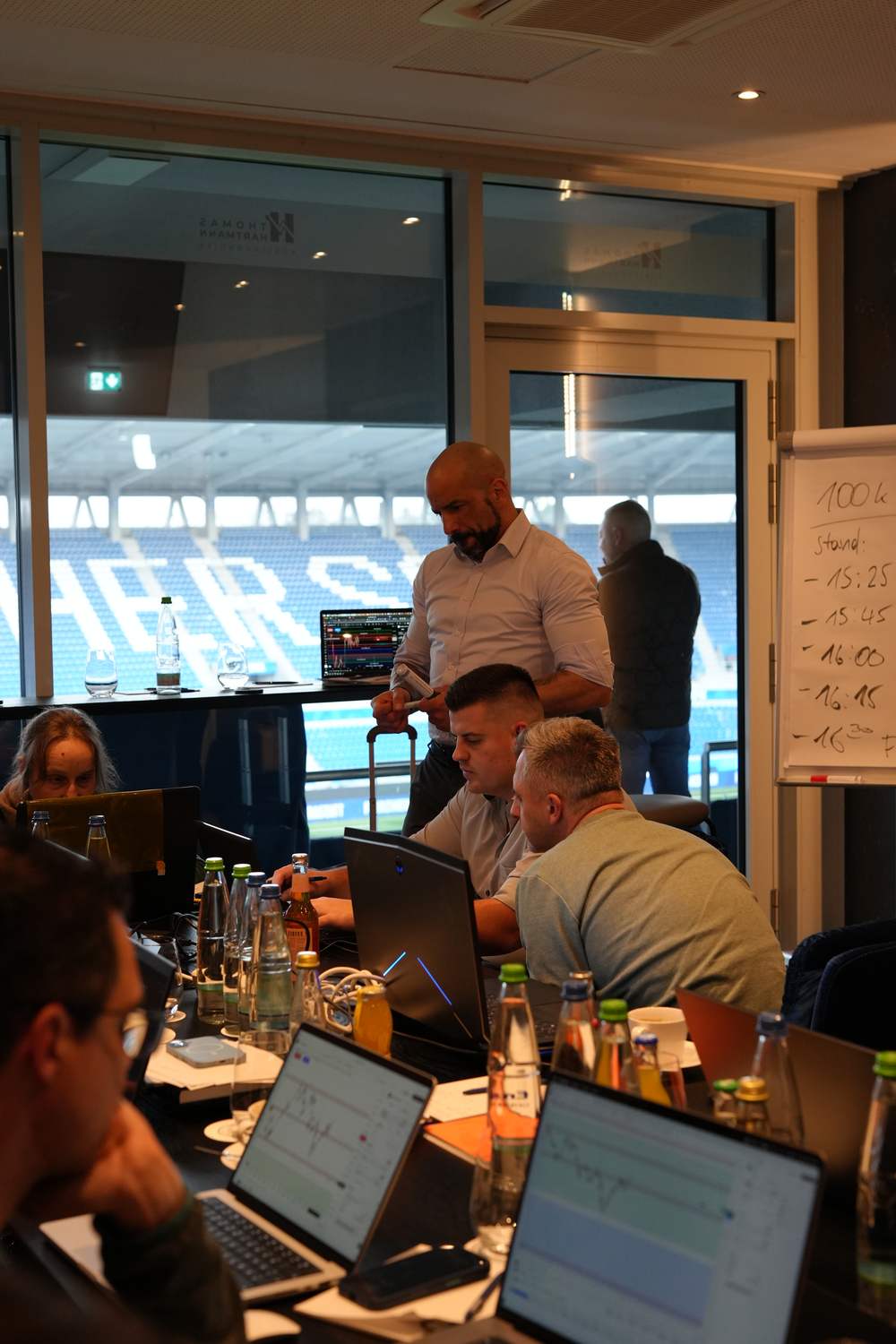 Thomas Hartmann am Tisch mit den Teilnehmern, im Hintergrund das Whiteboard mit dem Stand des Tages