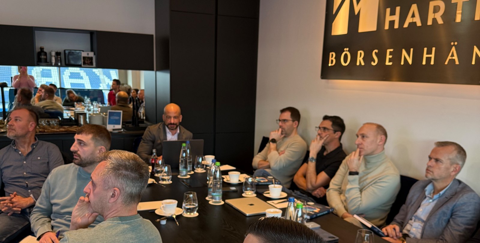 Teilnehmer des Bootcamps am Konferenztisch, konzentriert auf die Präsentation, im Hintergrund das Logo Thomas Hartmann Börsenhändler